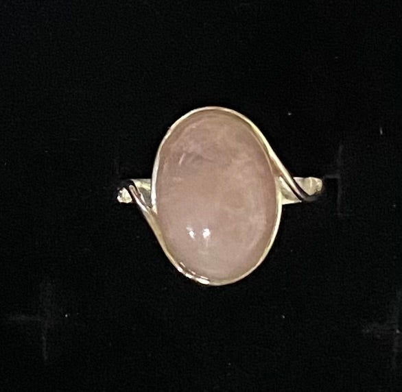 A silver ring featuring a large, smooth, oval-shaped pale pink stone, displayed against a solid black background.