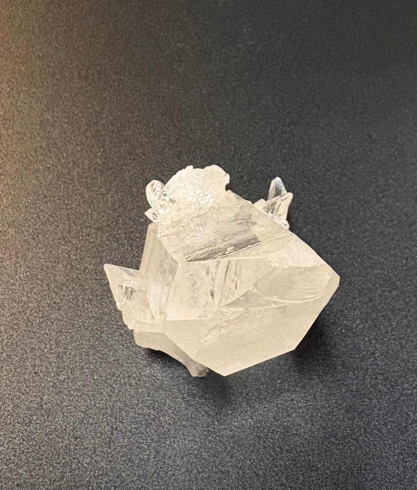 A natural clear quartz crystal point with rough, textured matrix base, photographed on a dark textured surface.