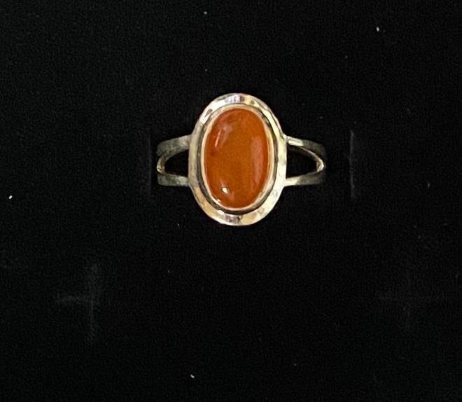 A silver ring with an oval cabochon orange stone, displayed on a black background.