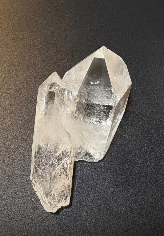 A clear quartz crystal cluster with natural inclusions, photographed on a dark textured background.
