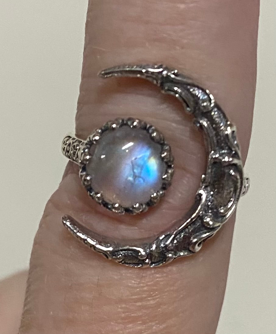 A silver crescent moon ring with a central round iridescent moonstone, shown worn on a finger.