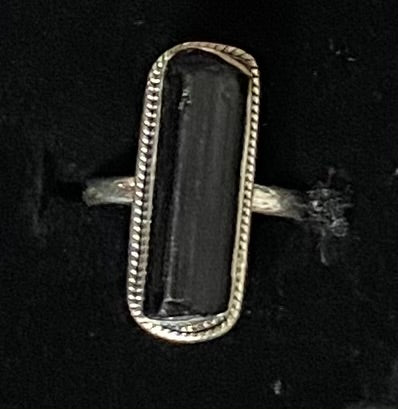 A silver-toned ring featuring a large, polished rectangular black gemstone, set against a dark black background.