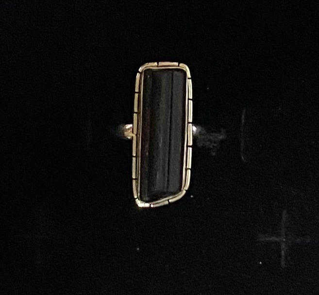 A rectangular gold ring featuring a dark, polished black stone, set against a solid black background.