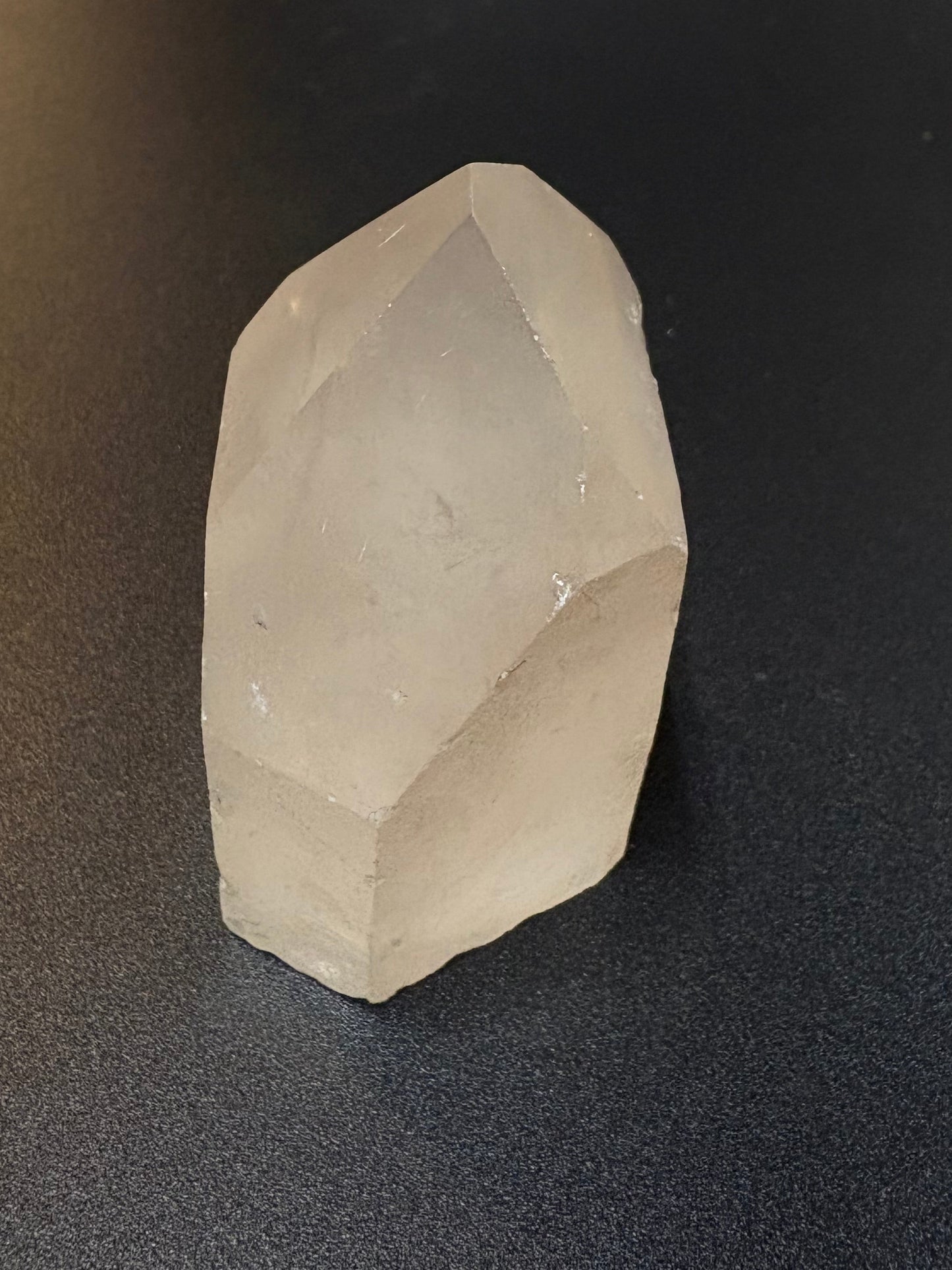 A faceted, translucent white crystal stone resting on a dark textured surface.