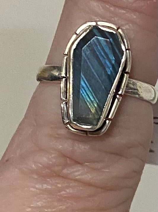 A silver ring with a large, irregular-cut blue iridescent labradorite gemstone, shown worn on a person's finger.