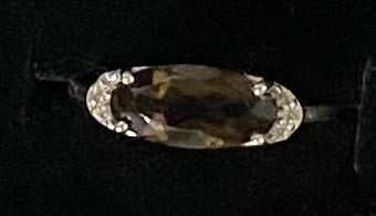 An oval-cut gemstone ring with a silver-toned setting, displayed on a black background.