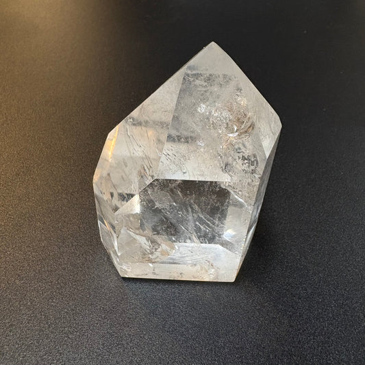 A clear quartz crystal point with natural inclusions, displayed on a dark textured surface.