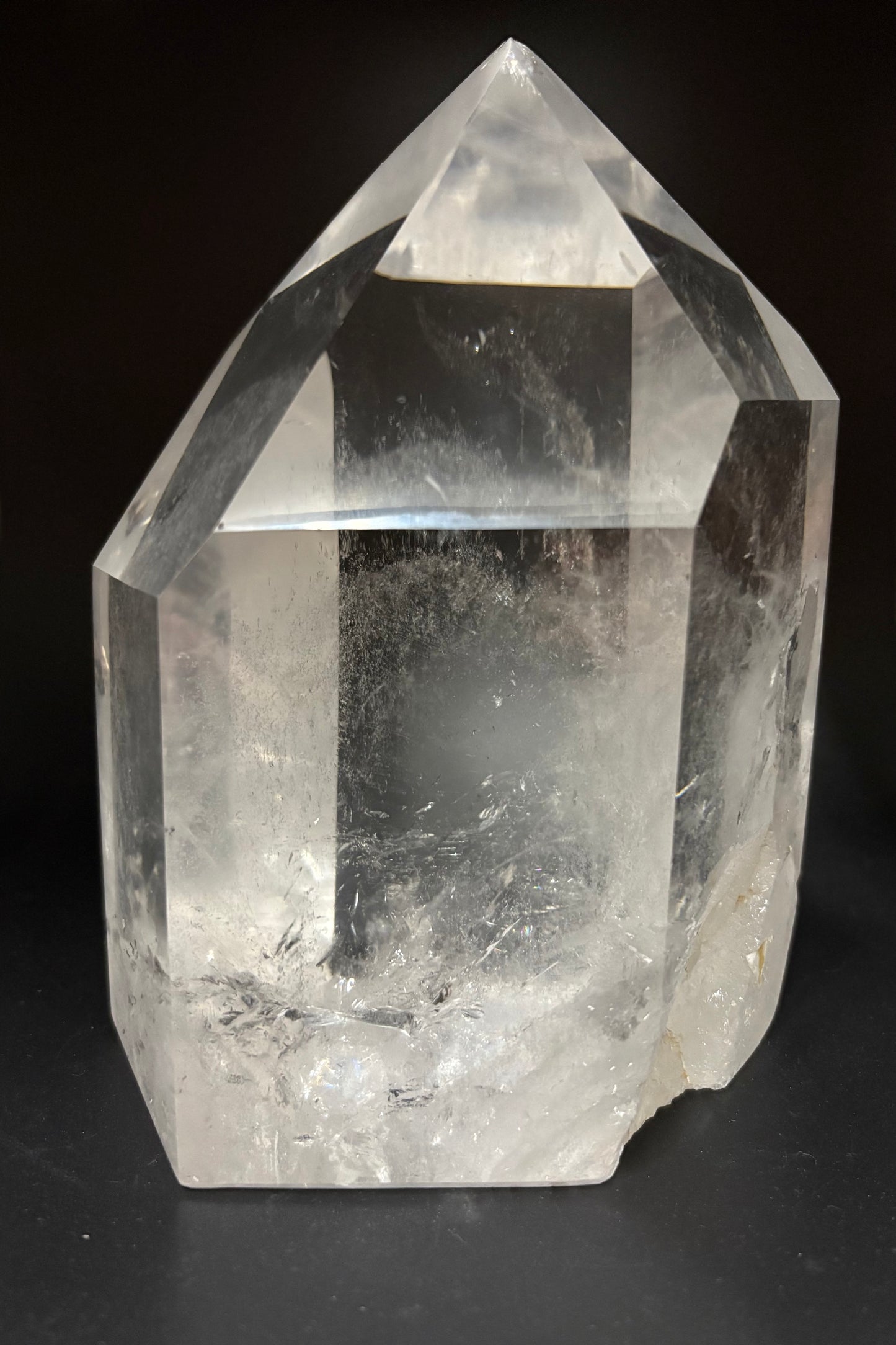 A natural clear quartz crystal point with sharp geometric facets and internal inclusions, photographed against a dark black background.