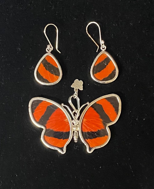 A jewelry set featuring a butterfly-shaped earring and a matching teardrop dangle earring, both decorated with vibrant orange and black striped butterfly wings set in silver-tone metal, displayed on a black background.
