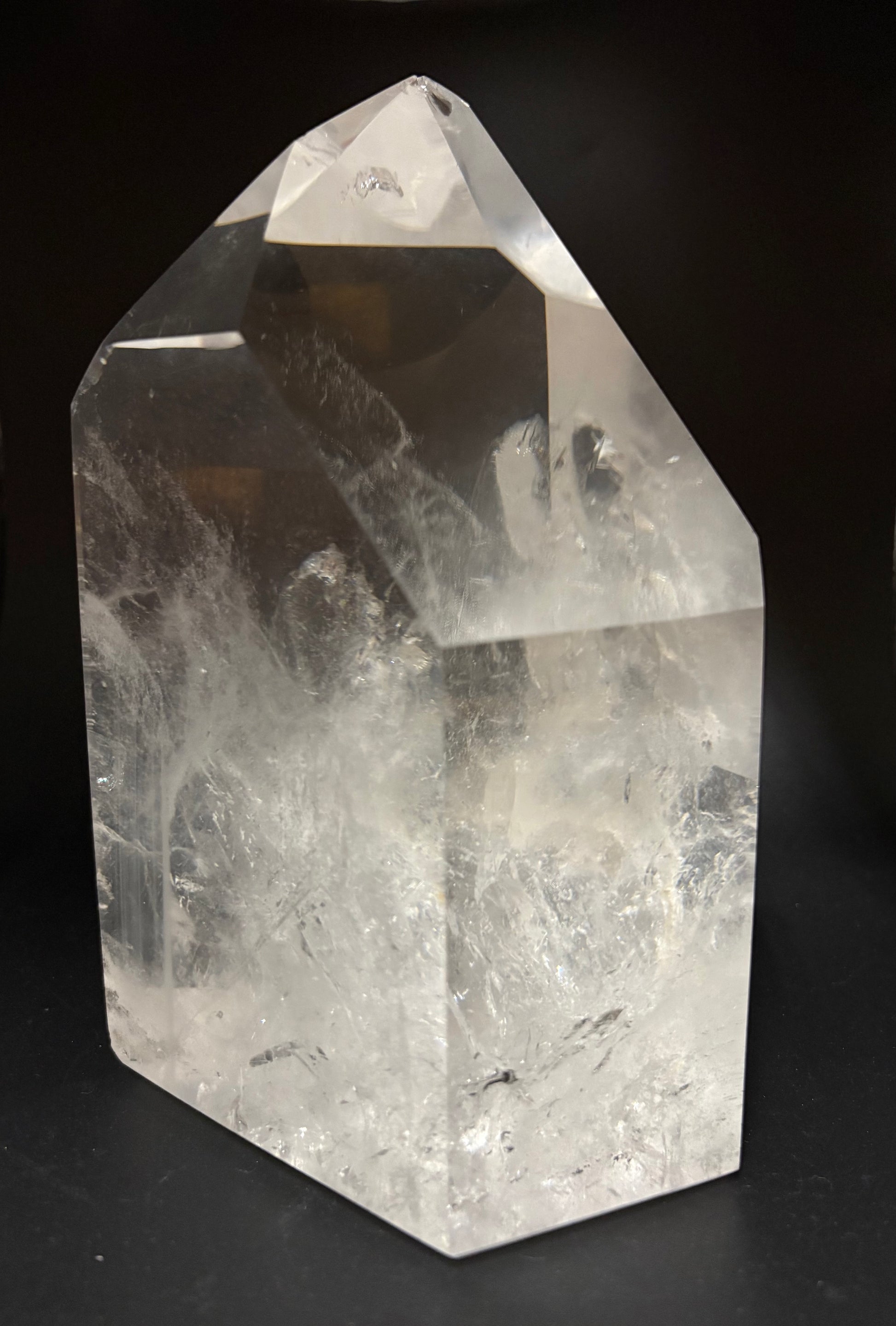 A clear quartz crystal point with natural inclusions and cloudy internal structure, photographed on a dark black background.