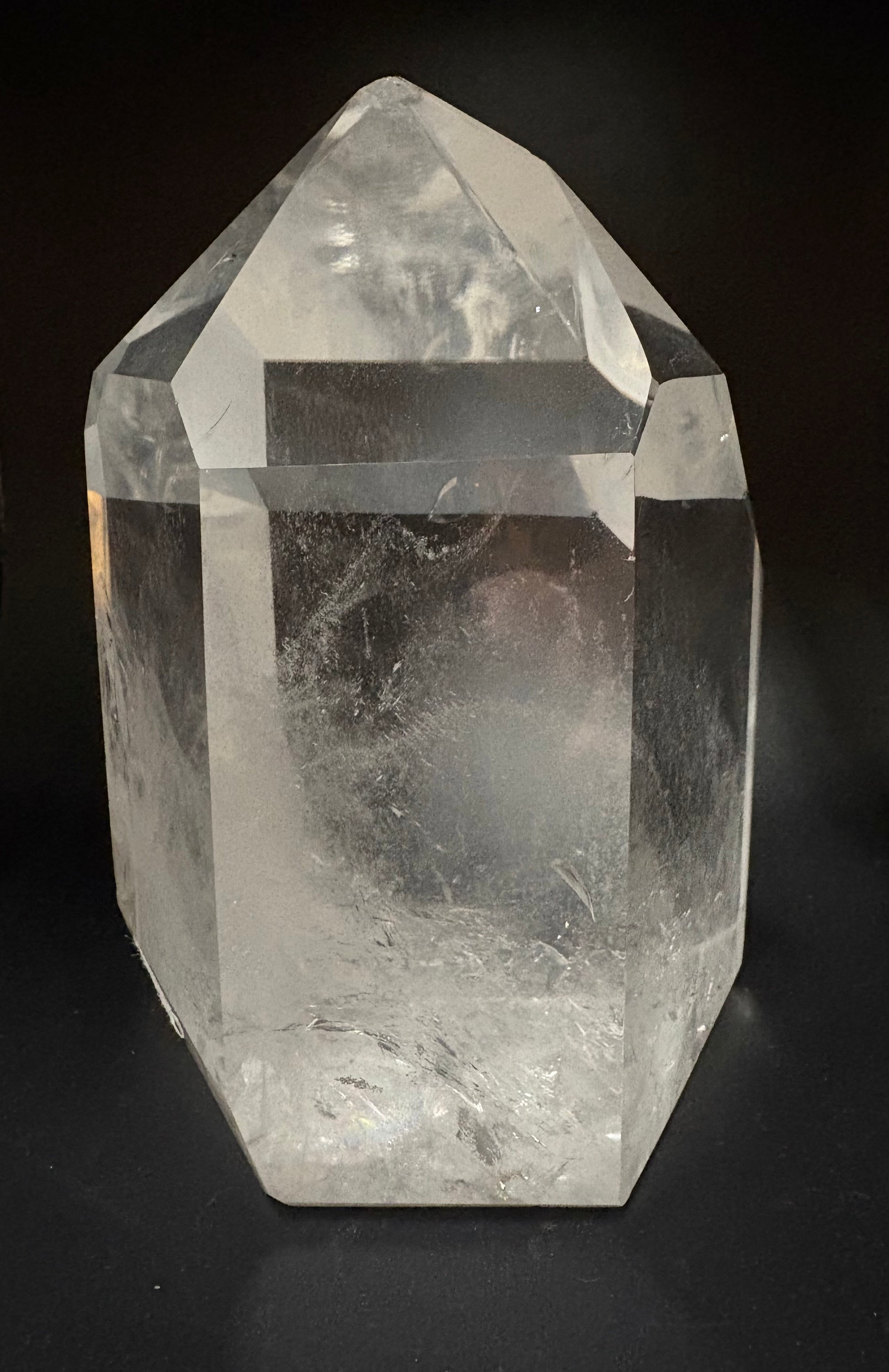 A clear quartz crystal point tower with natural inclusions, photographed against a solid black background.