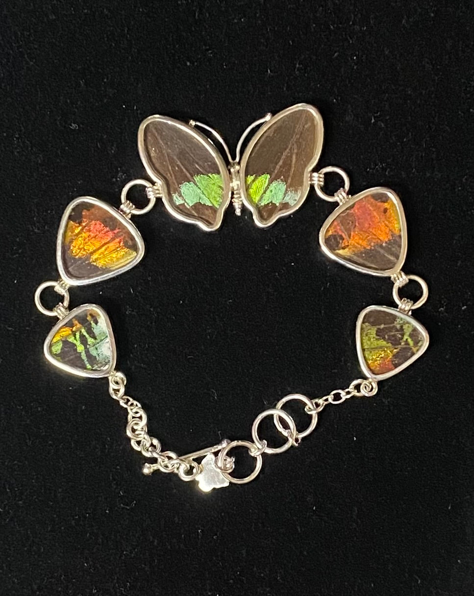 A silver chain bracelet featuring butterfly wings and guitar-pick-shaped inlays with colorful iridescent inclusions, displayed on a black background.