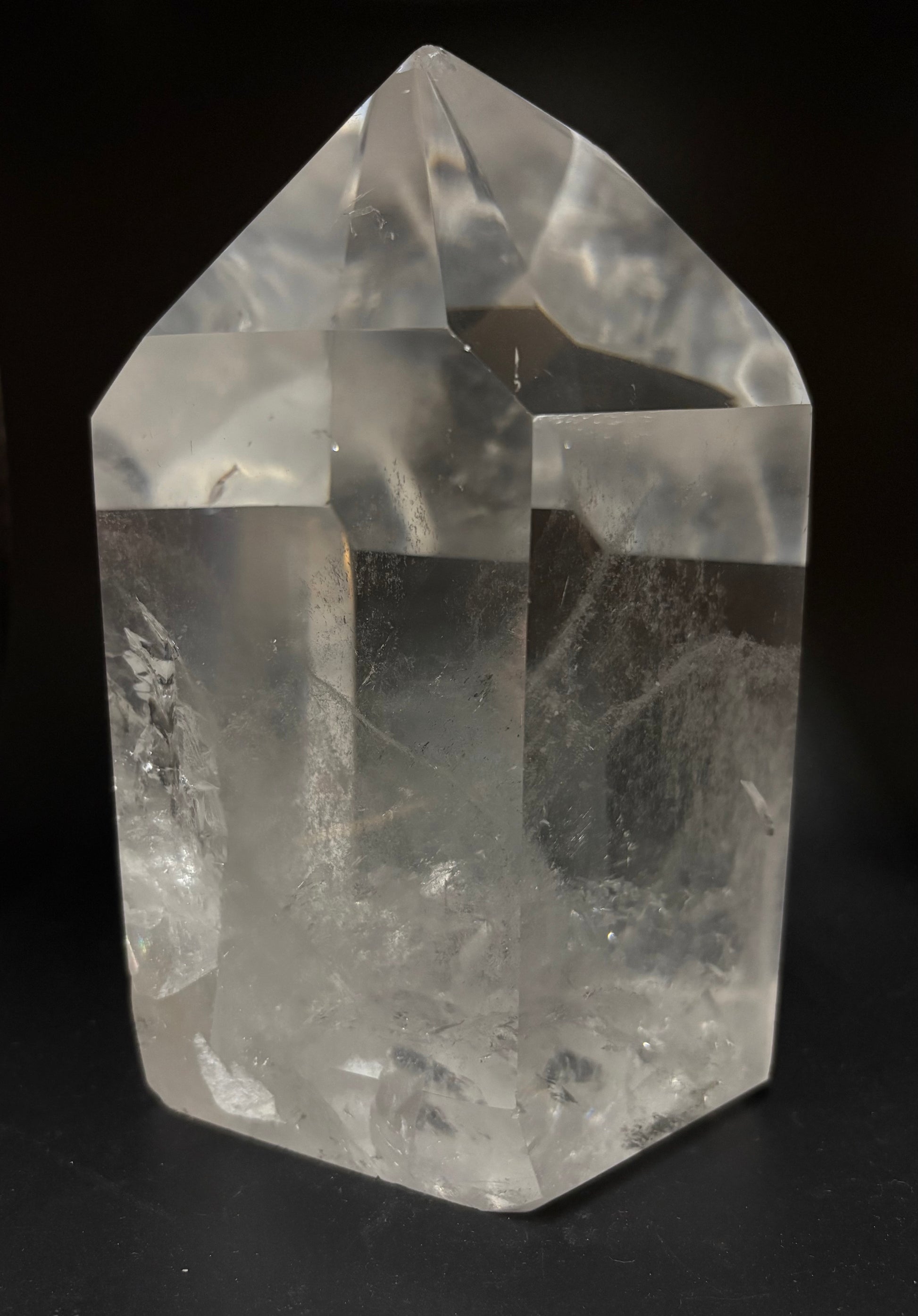 A clear quartz crystal point tower with natural inclusions, photographed against a solid black background.