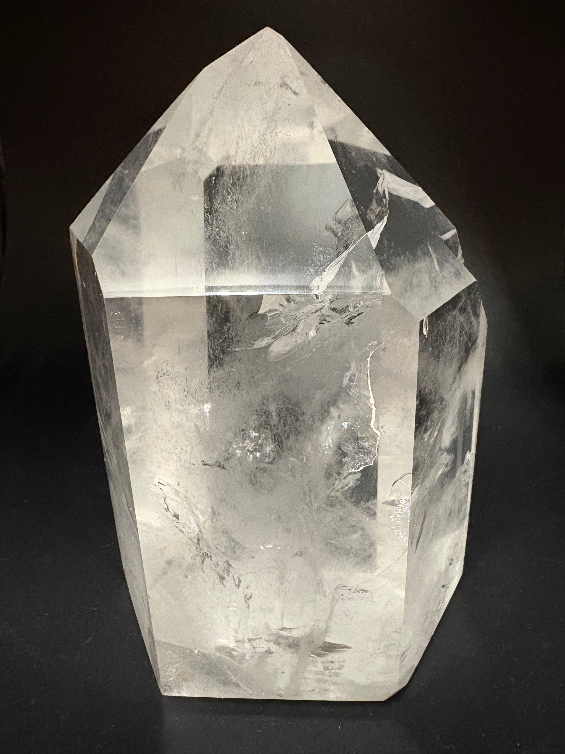 A clear quartz crystal point with natural inclusions and fractures, photographed on a dark black background.