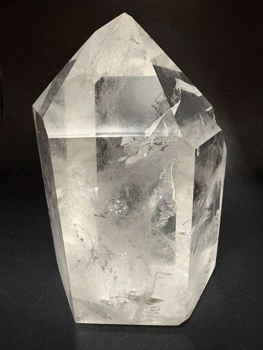 A clear quartz crystal point with natural inclusions and fractures, photographed on a dark black background.