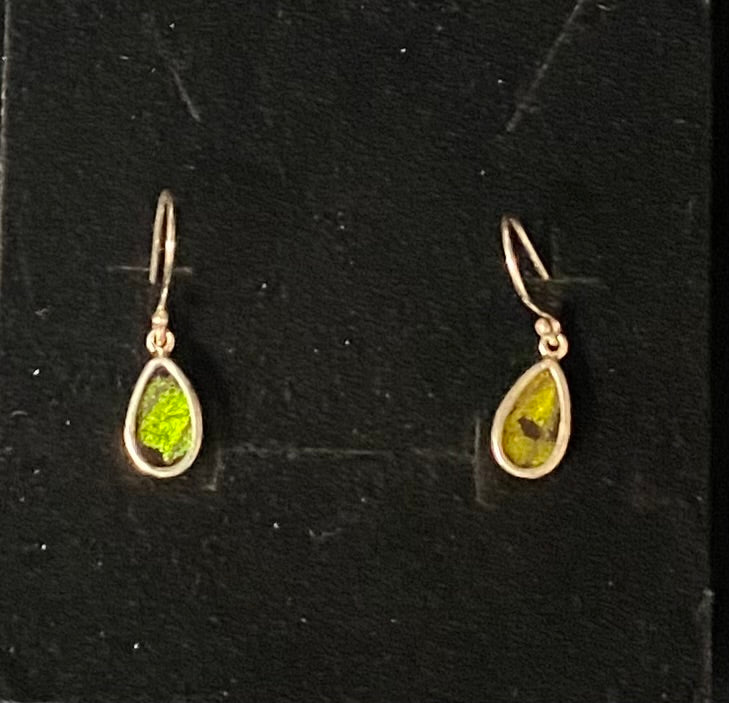 A pair of sterling silver teardrop dangle earrings with bright green stones, displayed on a black textured background.