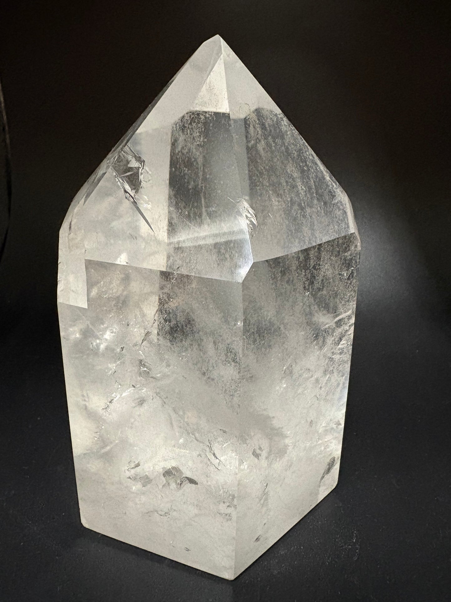 A clear faceted crystal point, likely quartz, displayed on a dark black background.