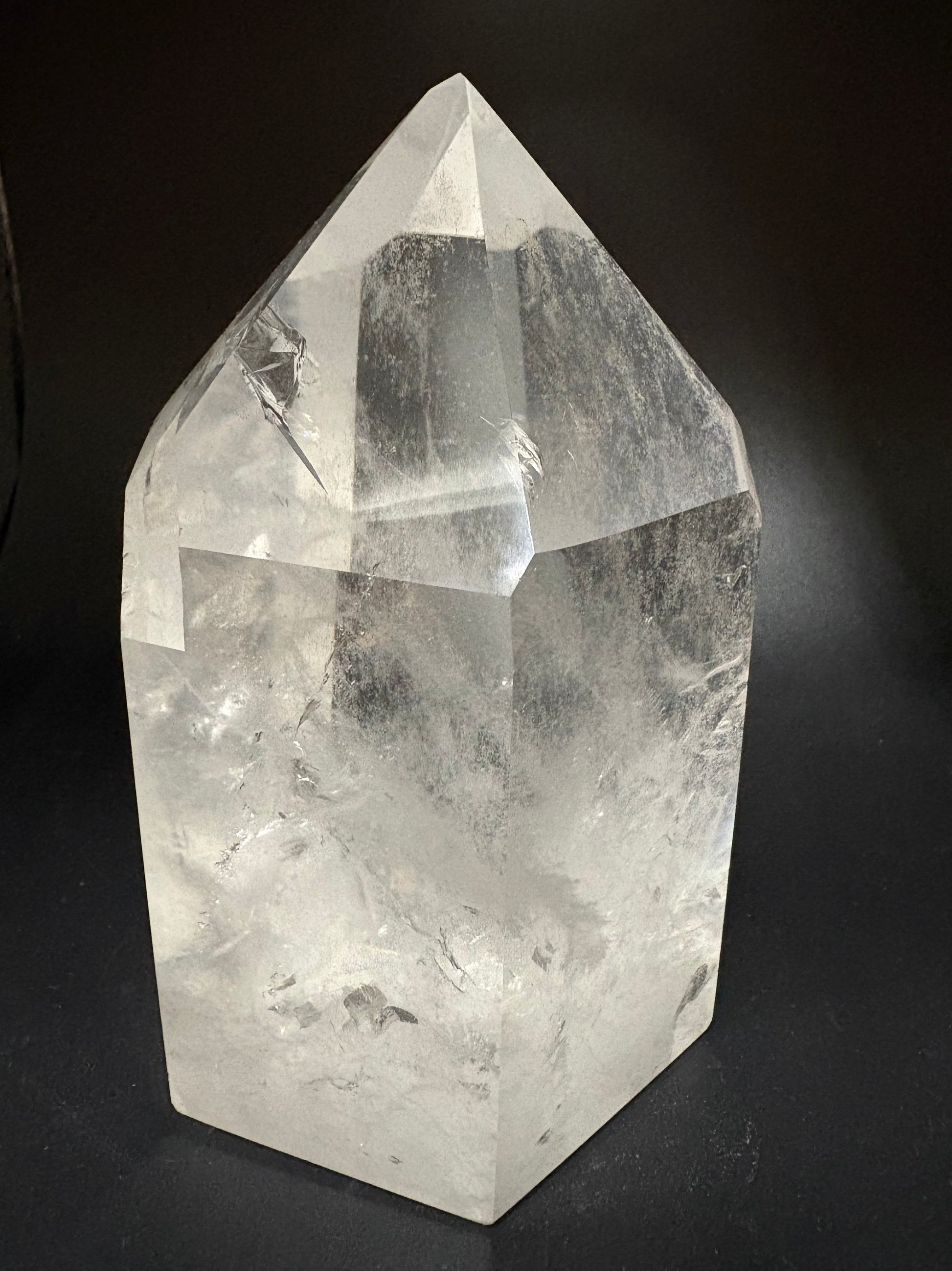 A clear faceted crystal point, likely quartz, displayed on a dark black background.