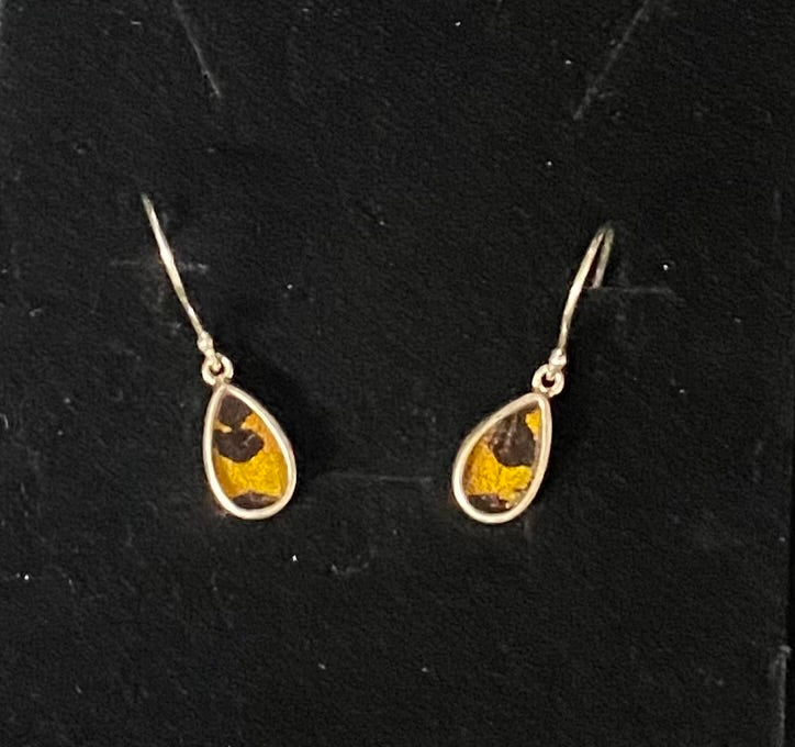 A pair of teardrop-shaped dangle earrings with yellow and black patterned inlay, set in a silver-tone metal and suspended from matching silver-tone fishhook wires, displayed on a black textured background.