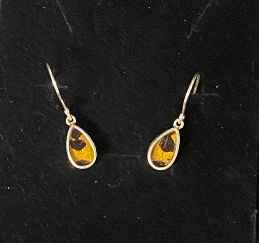 A pair of teardrop-shaped dangle earrings with yellow and black patterned inlay, set in a silver-tone metal and suspended from matching silver-tone fishhook wires, displayed on a black textured background.