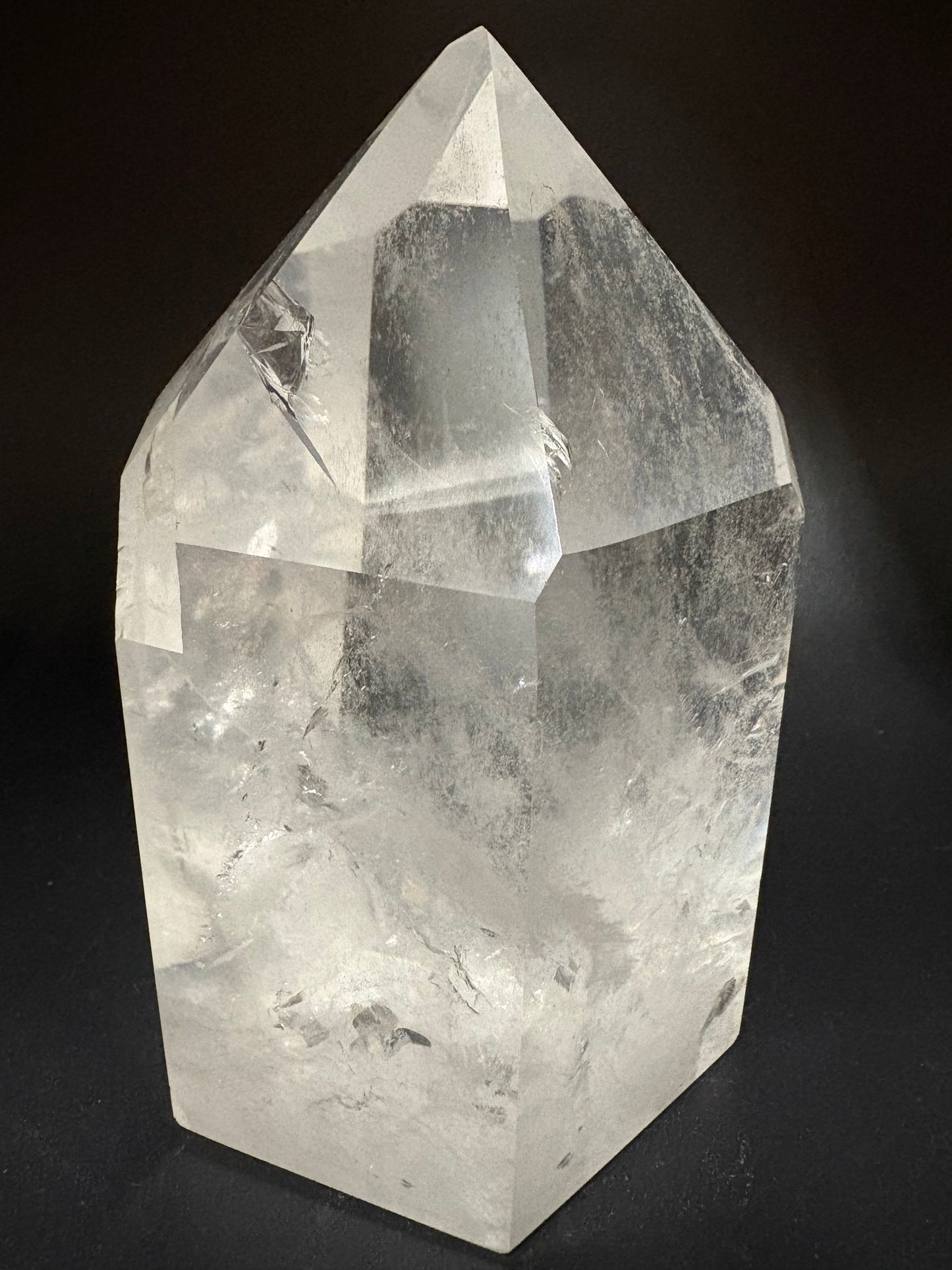A large, natural clear quartz crystal point with visible internal inclusions and cloudy texture, photographed against a solid black background.