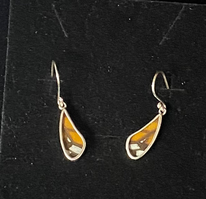 A pair of teardrop-shaped dangle earrings with a silver-tone metal frame and a central amber-brown butterfly wing inlay, displayed on a black velvet jewelry stand.