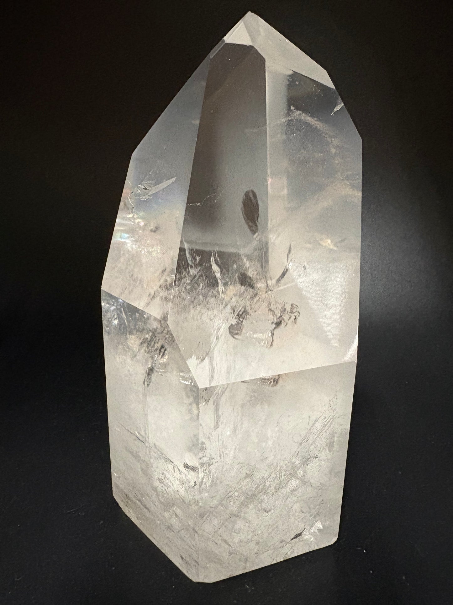 A clear quartz crystal point with visible internal inclusions, photographed on a dark black background.