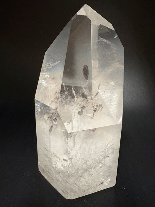A clear quartz crystal point with visible internal inclusions, photographed on a dark black background.