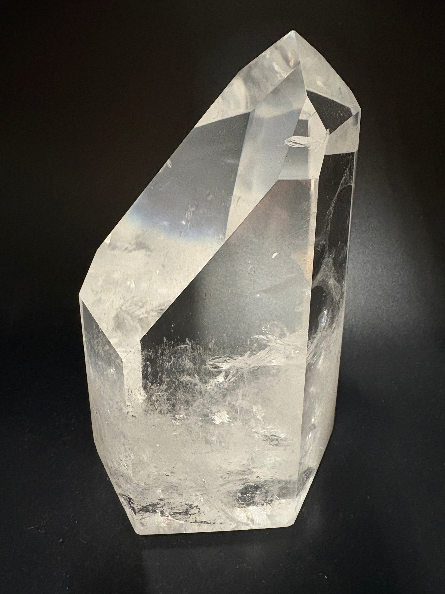 A faceted clear quartz crystal point with natural inclusions, photographed on a dark black background.