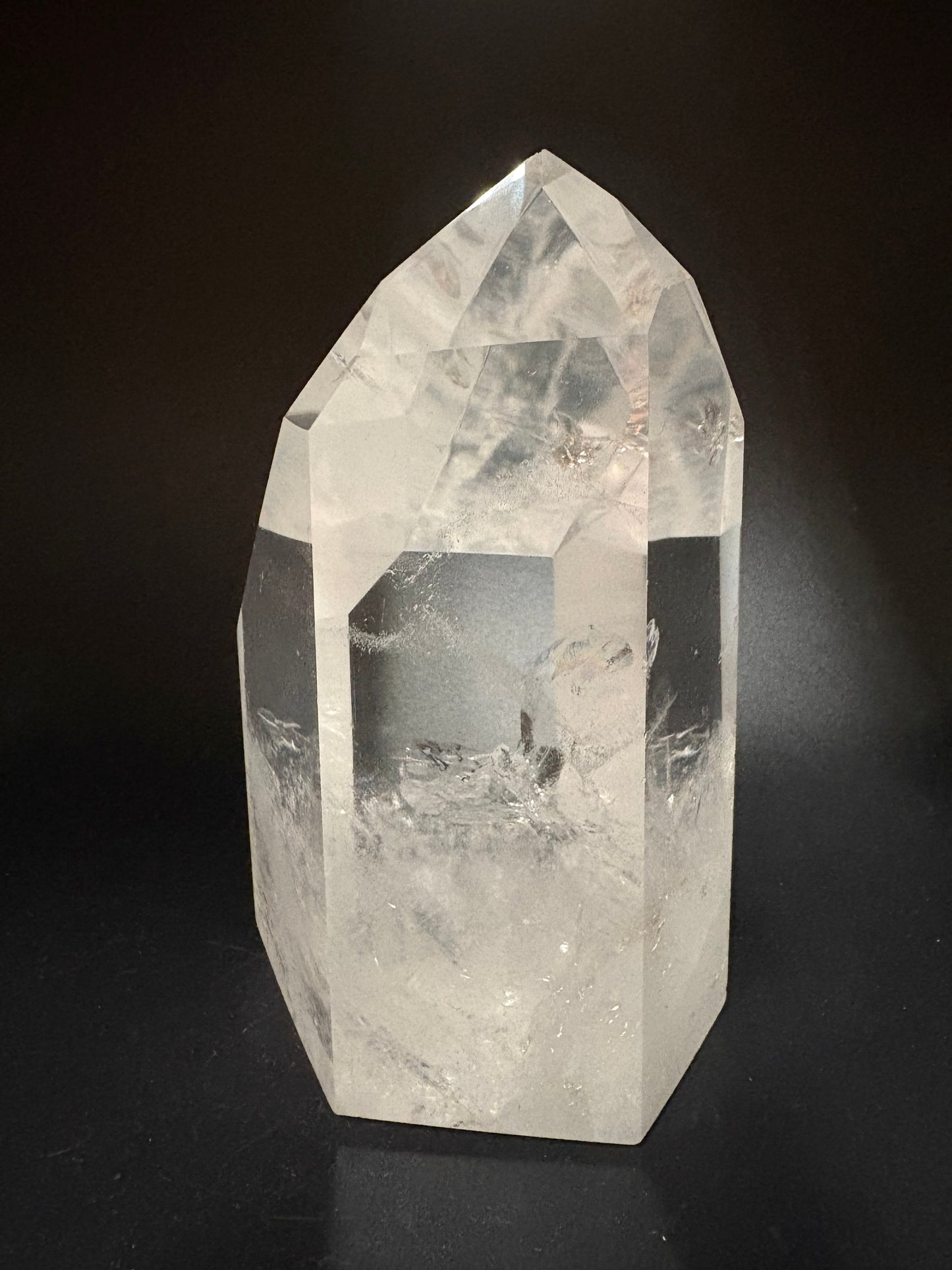 A clear quartz crystal point with natural inclusions, photographed on a dark black background.
