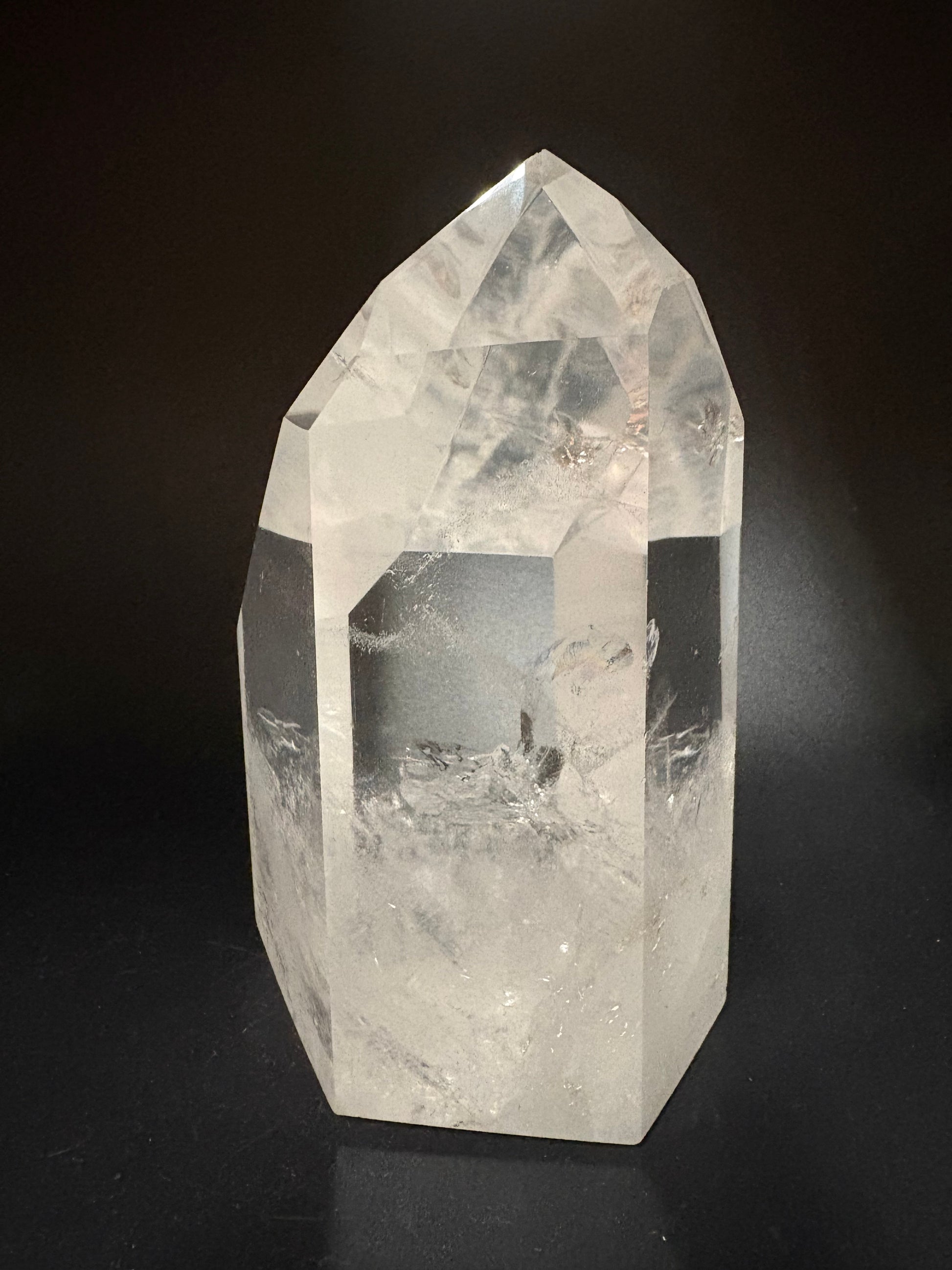 A clear quartz crystal point with natural inclusions, photographed on a dark black background.