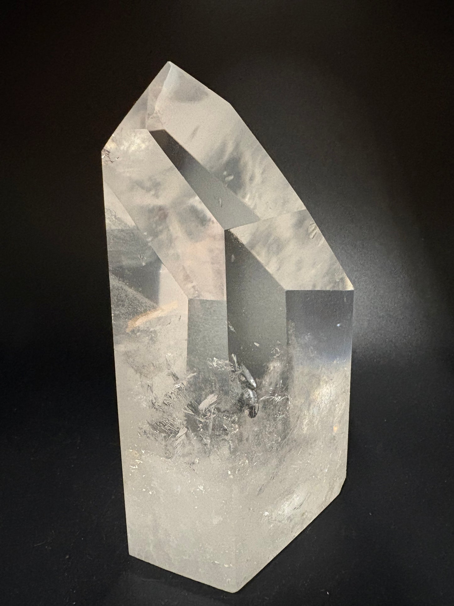 A clear quartz crystal point with natural inclusions, photographed on a dark black background.