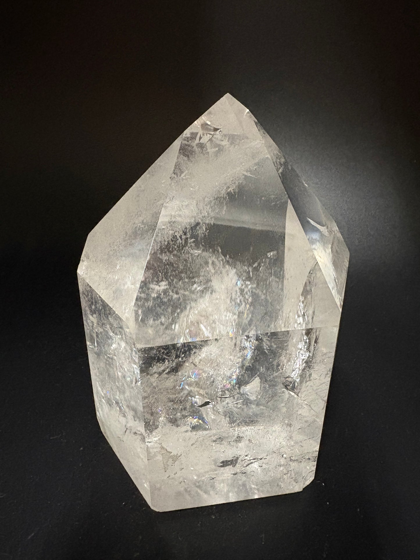 A raw, faceted clear quartz crystal with natural inclusions, displayed on a dark black background.