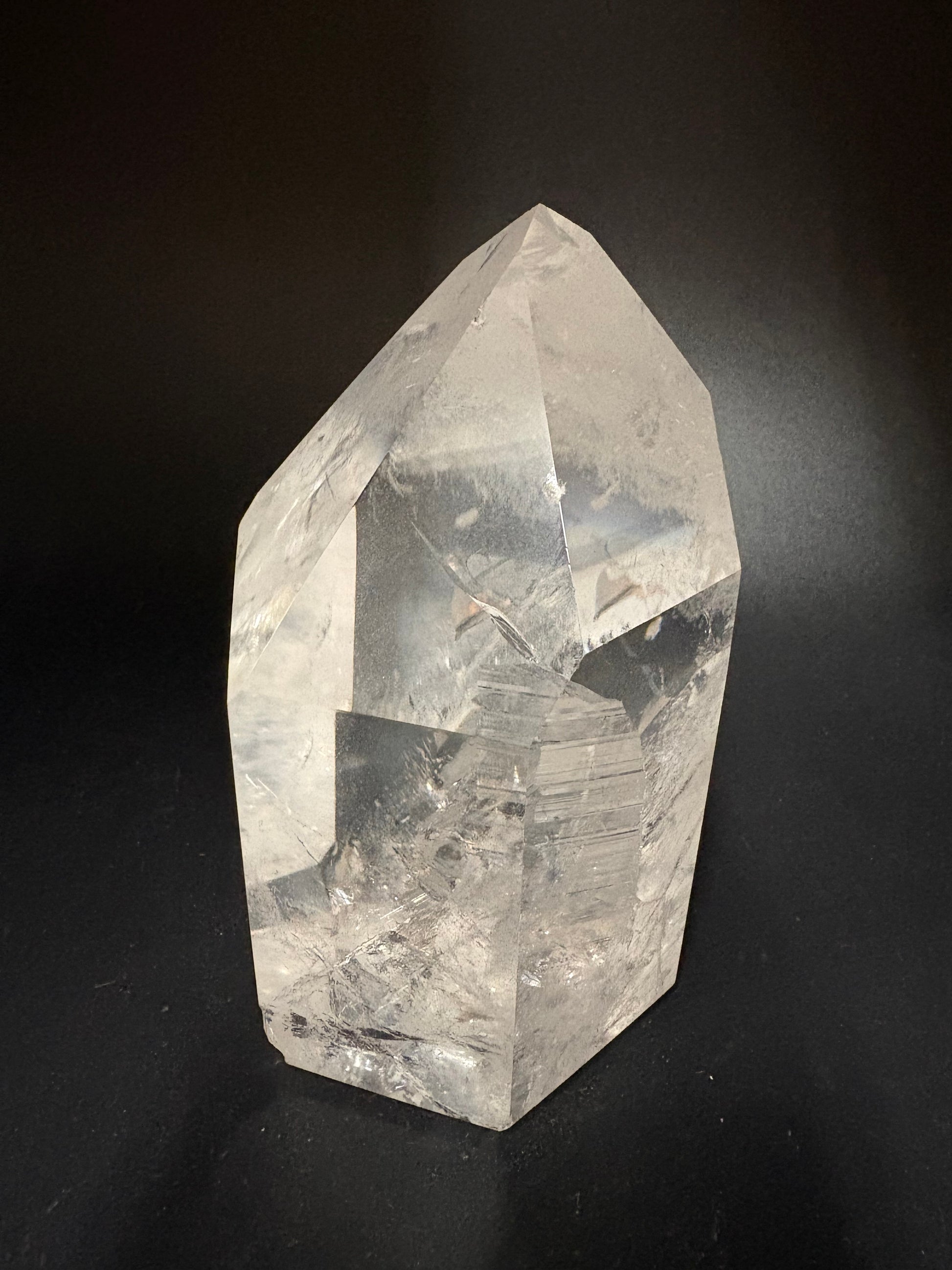 A clear faceted crystal stone with natural internal inclusions, photographed on a dark black background.