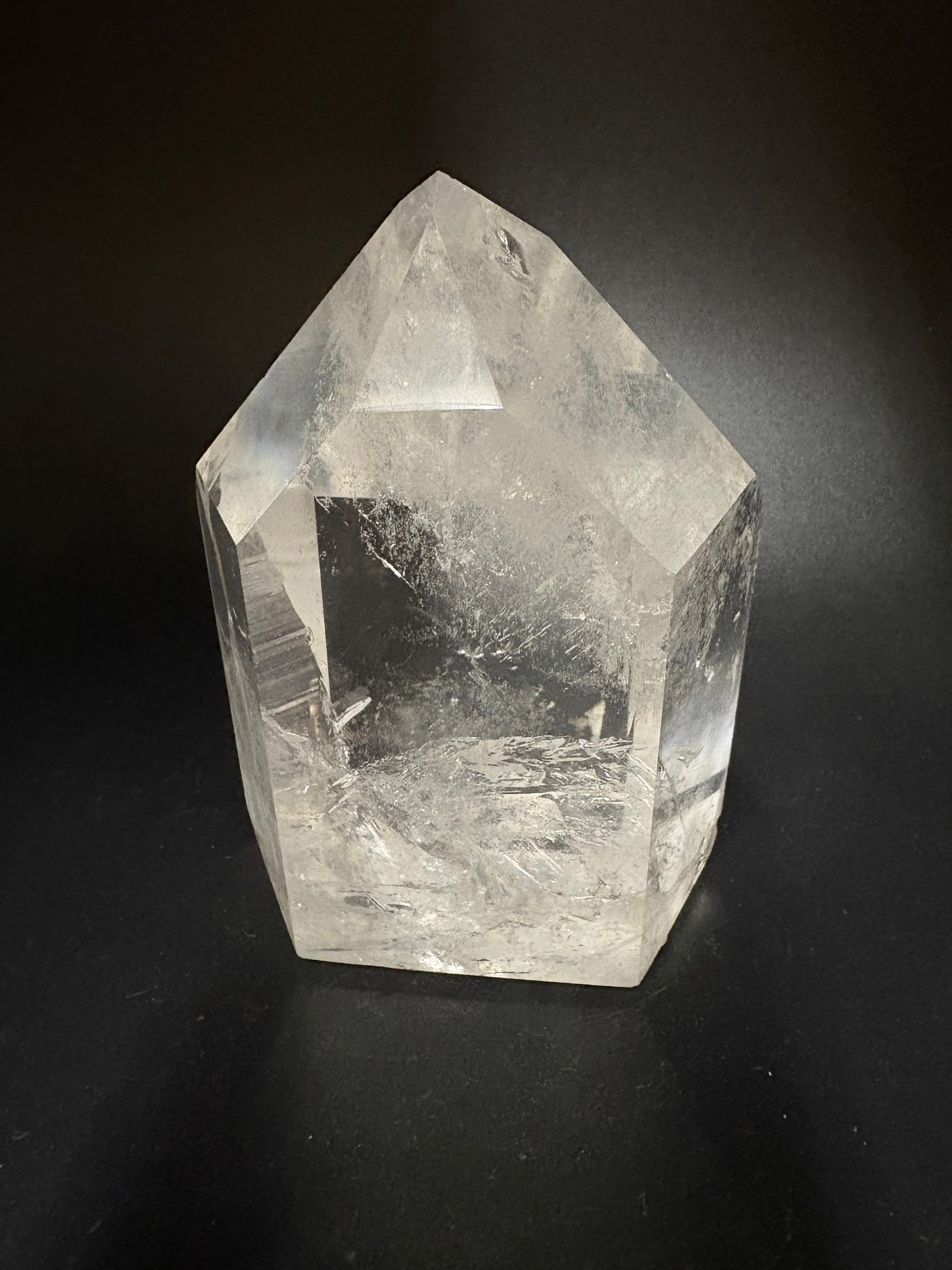 A raw, unpolished clear quartz crystal point with natural inclusions, displayed on a dark black background.