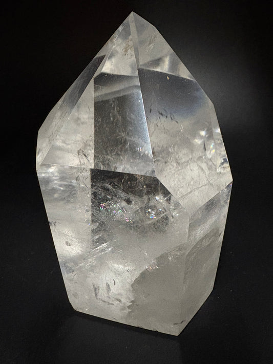 A large, faceted clear quartz crystal with natural inclusions, photographed on a solid black background.
