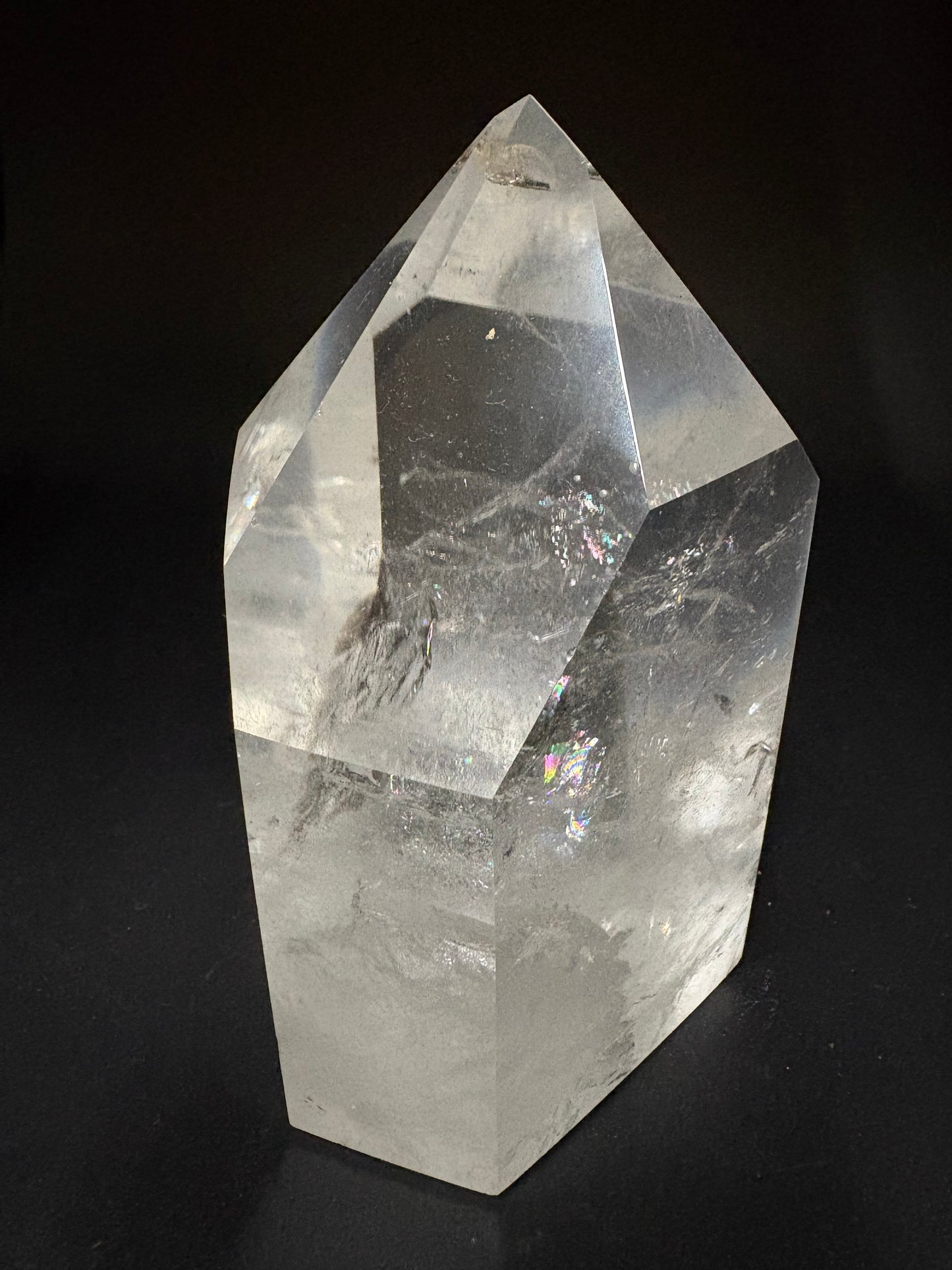 A large, clear natural quartz crystal point with visible internal inclusions and facets, photographed against a solid black background.