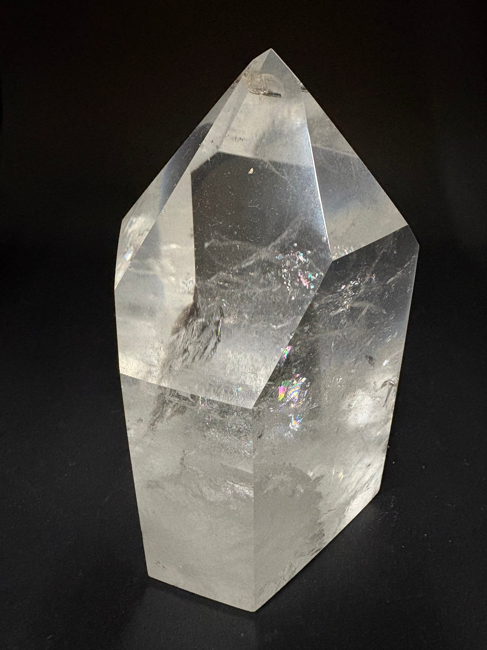 A large, clear natural quartz crystal point with visible internal inclusions and facets, photographed against a solid black background.