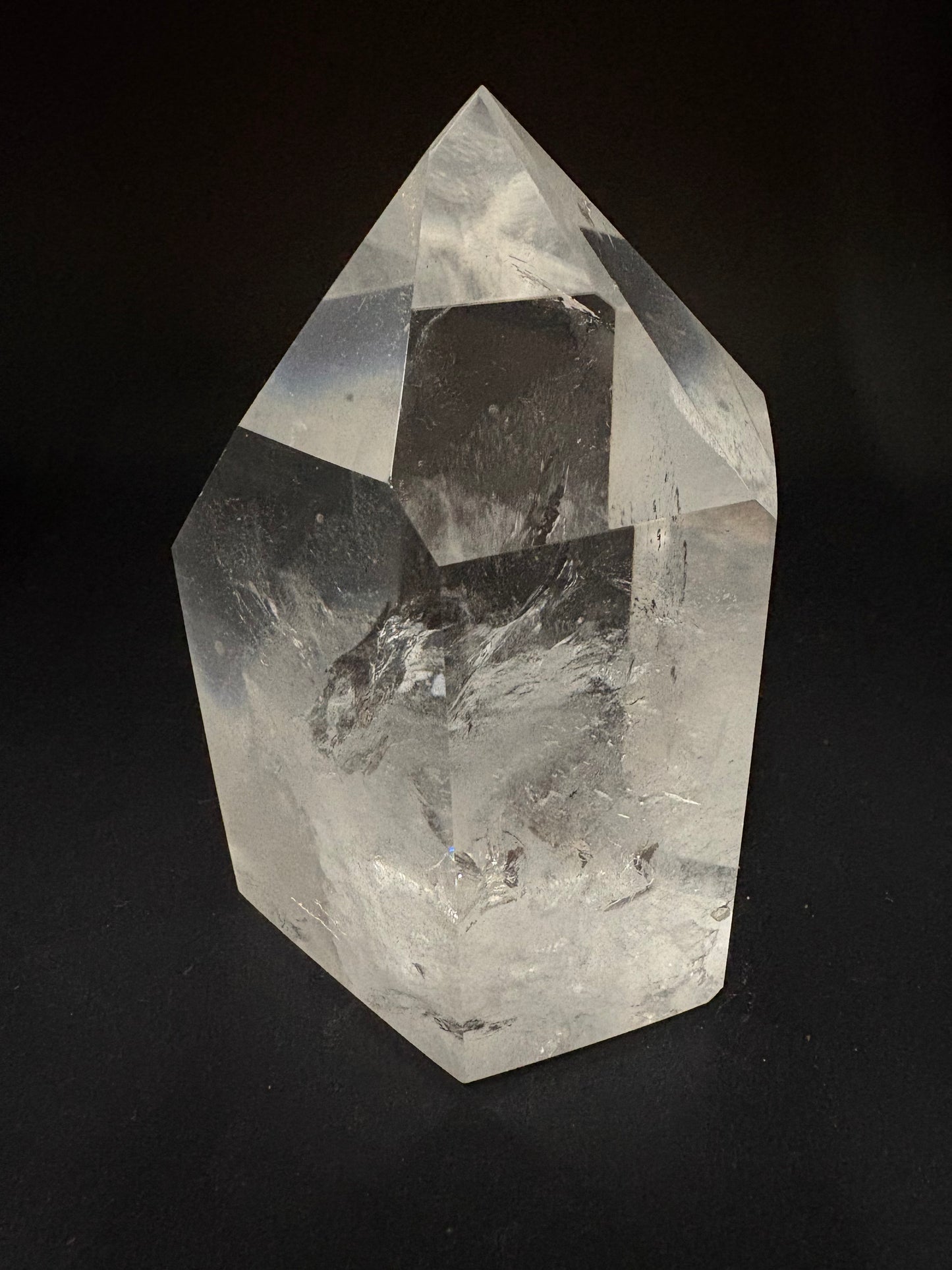 A clear faceted crystal stone with natural internal inclusions, photographed against a solid black background.