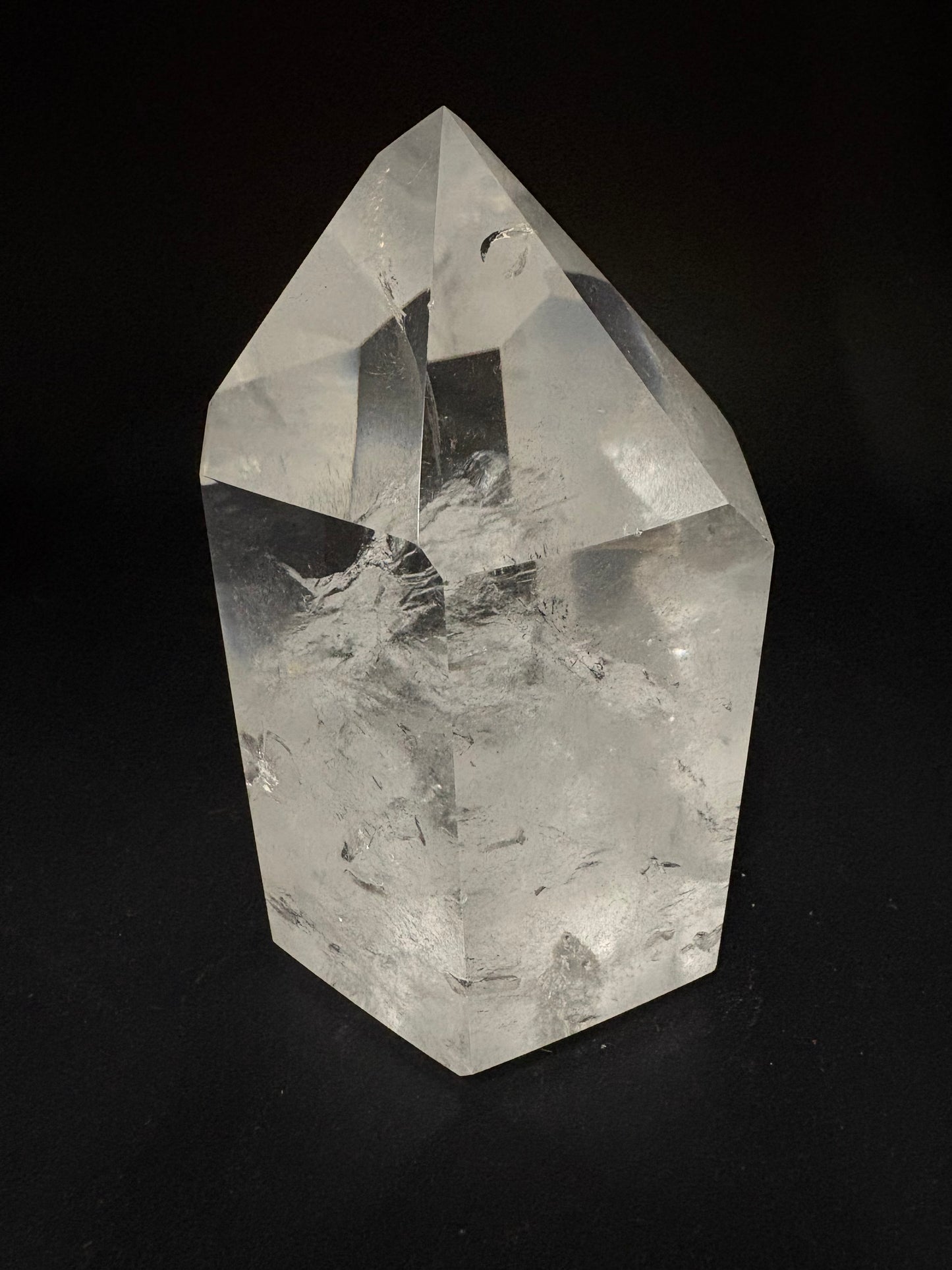 A faceted clear quartz crystal point with natural inclusions, displayed on a solid black background.