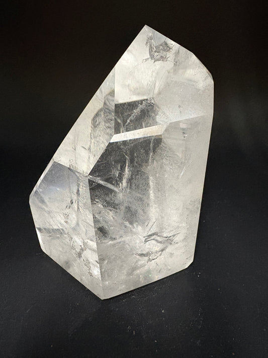 A faceted clear quartz crystal stone with natural inclusions, photographed on a dark black background.
