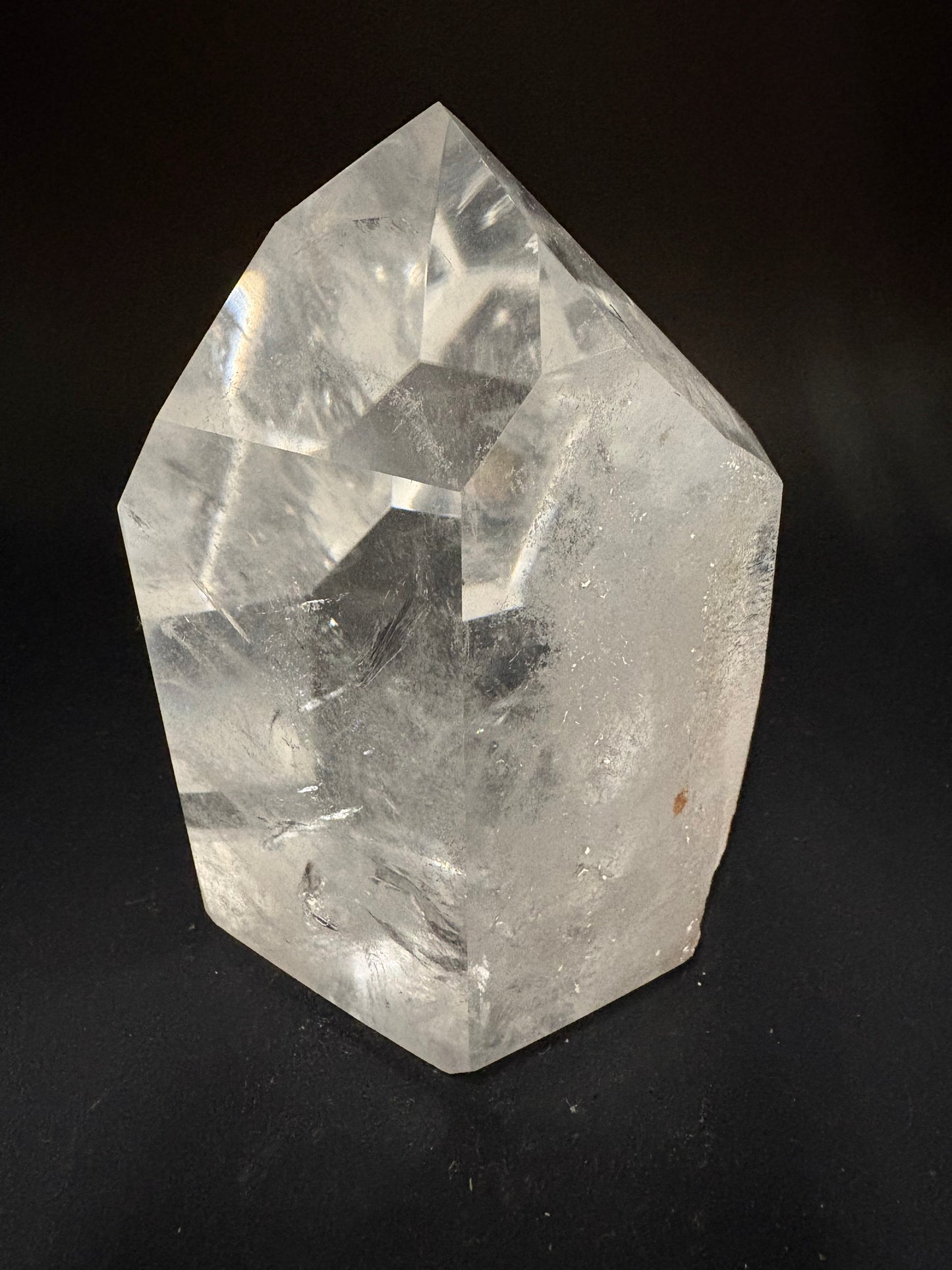 A raw, uncut clear quartz crystal with natural facets and internal inclusions, photographed on a solid black background.
