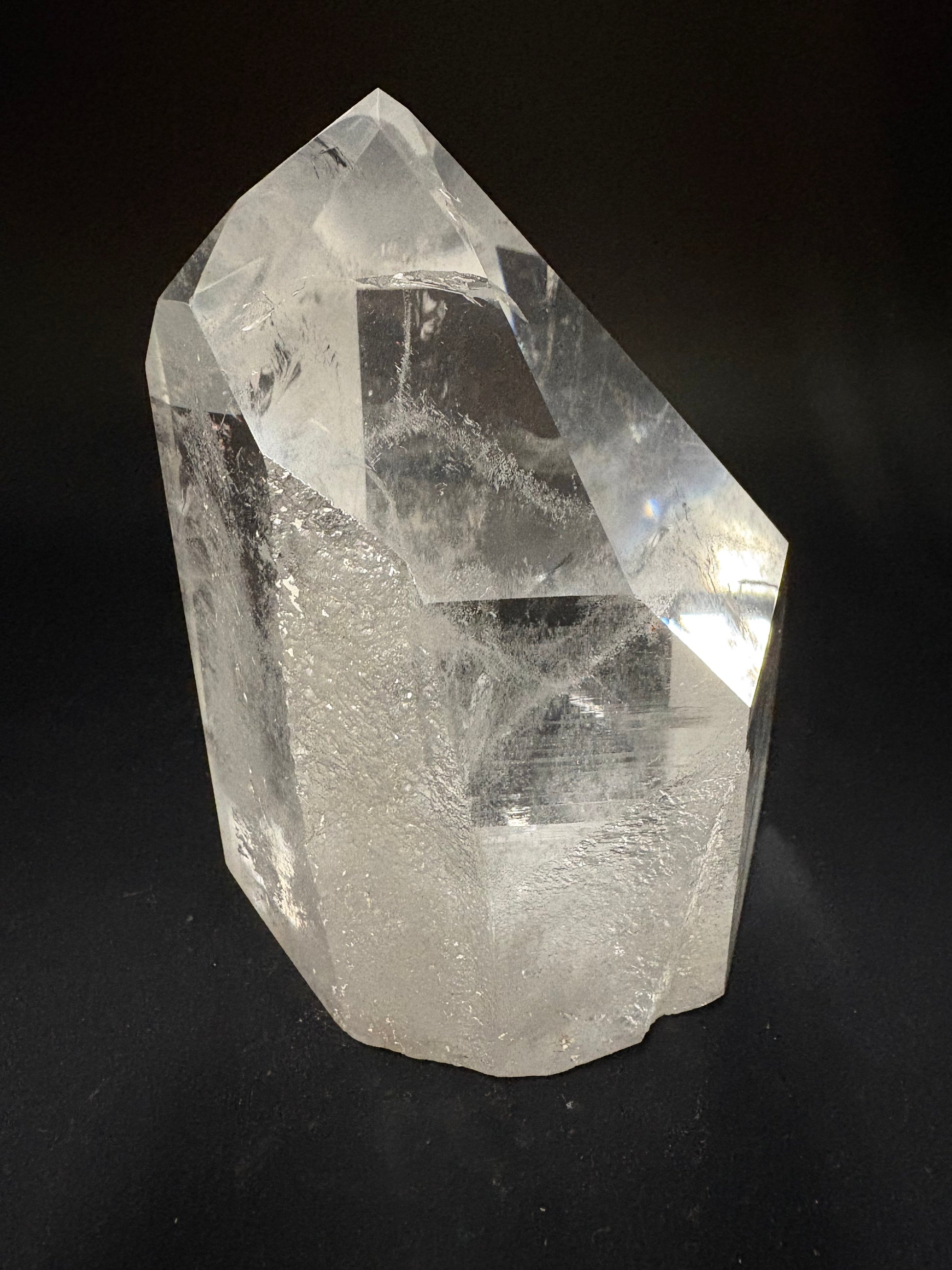 A raw, unpolished clear quartz crystal point with natural inclusions, displayed on a solid black background.