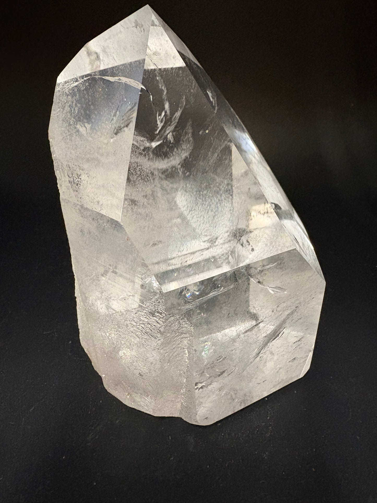 A raw, unpolished clear quartz crystal point with natural facets and internal inclusions, photographed on a dark black background.