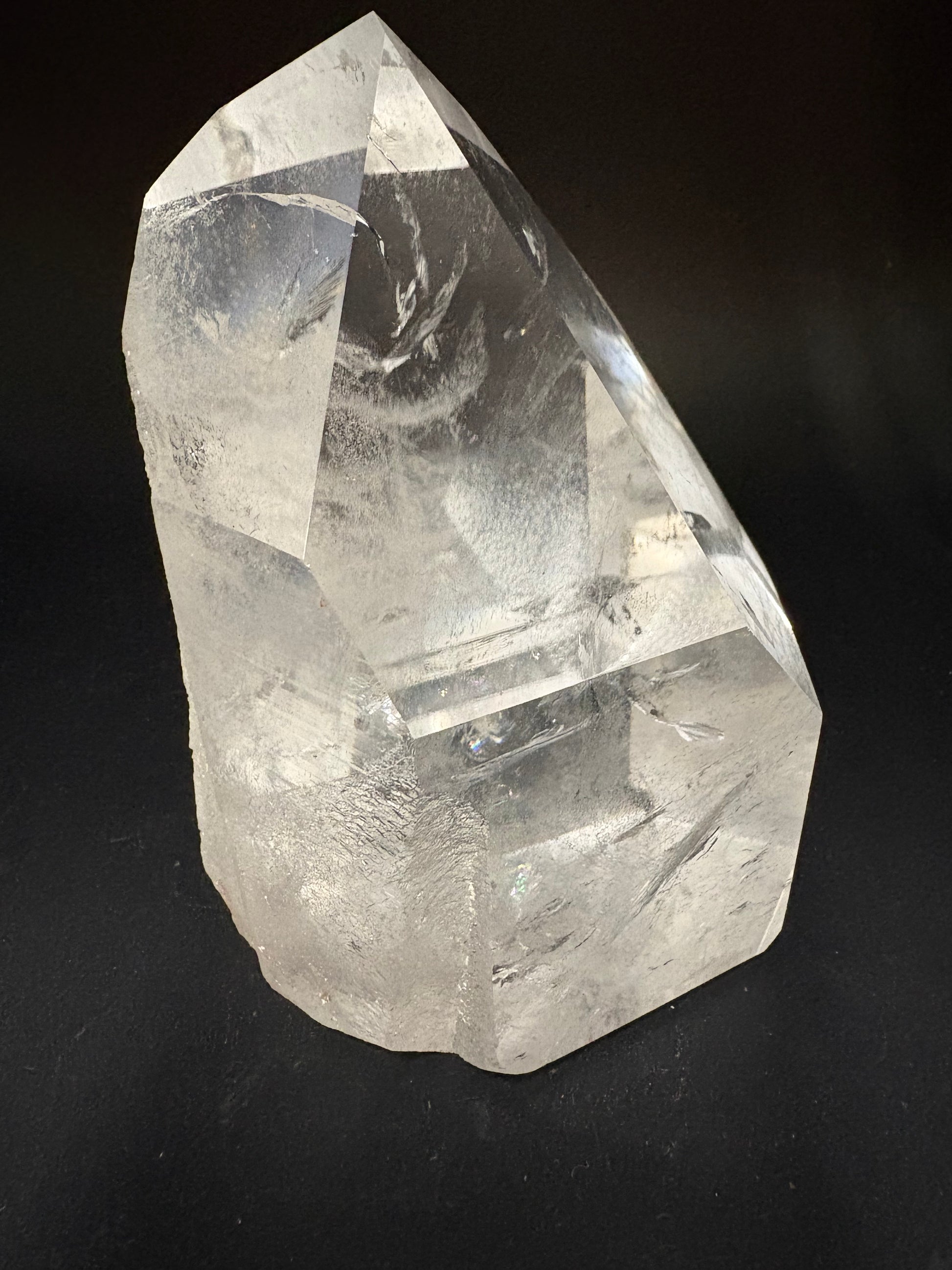 A raw, unpolished clear quartz crystal point with natural facets and internal inclusions, photographed on a dark black background.