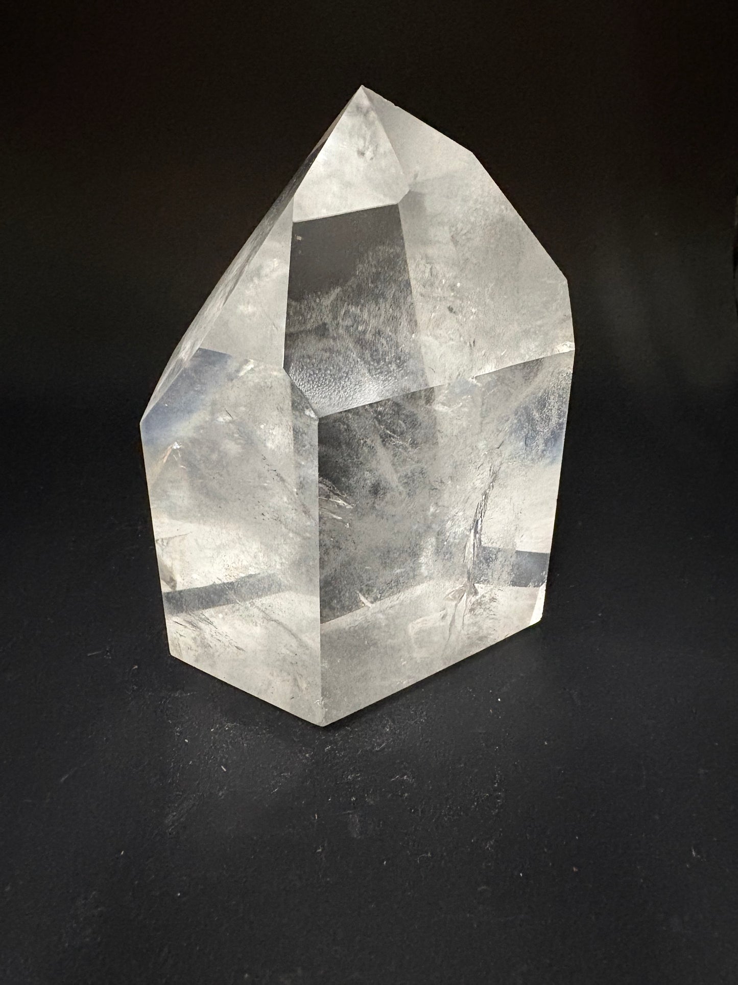 A faceted clear crystal stone, resembling a raw quartz point, displayed on a dark black background.