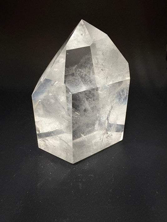 A faceted clear crystal stone, resembling a raw quartz point, displayed on a dark black background.
