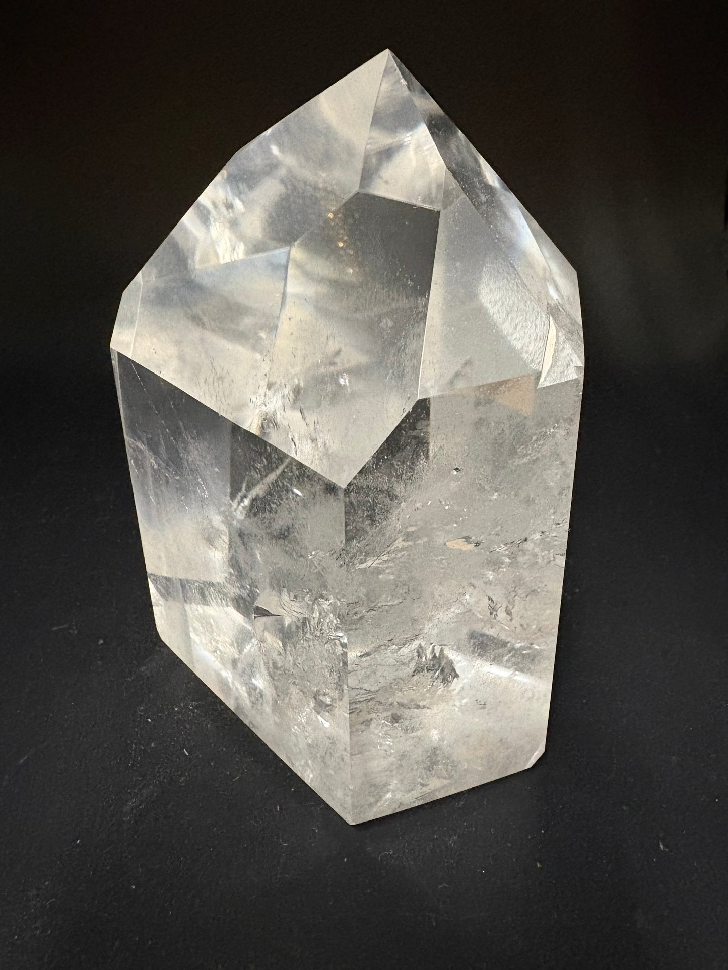 A faceted clear quartz crystal with natural inclusions, photographed on a dark black background.