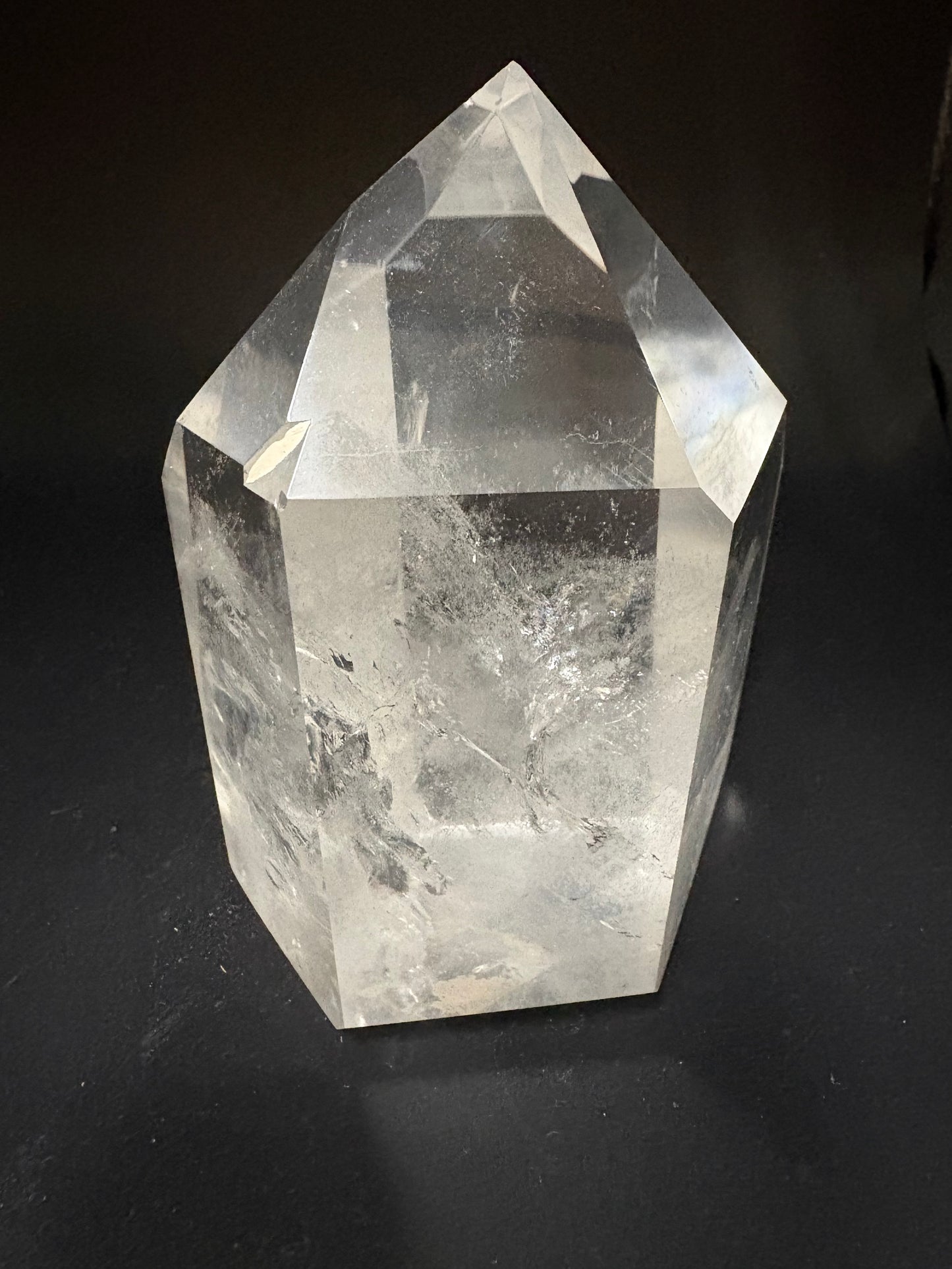 A clear faceted crystal point, likely quartz, displayed on a dark black background.