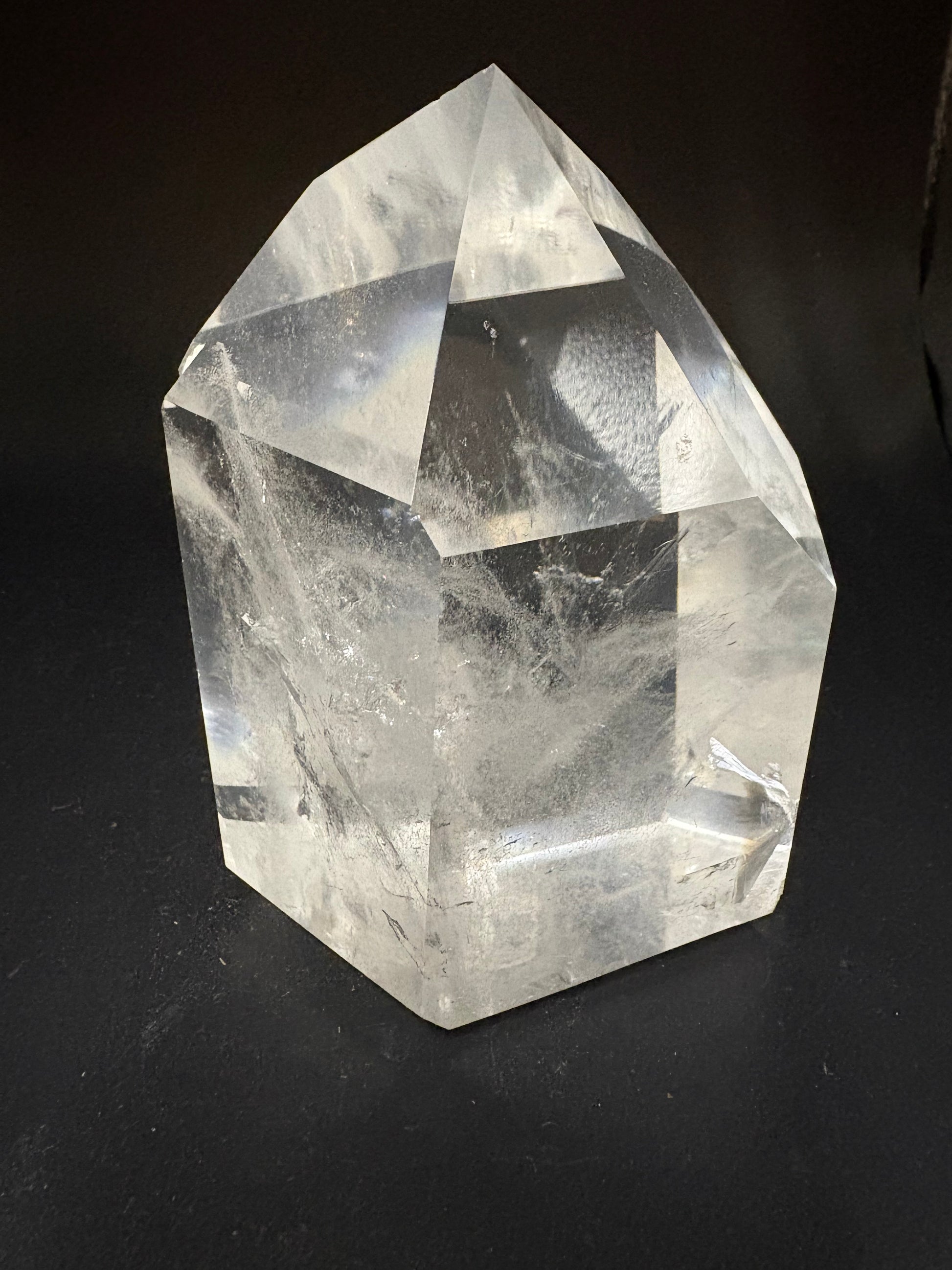 A large, faceted clear crystal stone, likely quartz, resting on a dark black background.